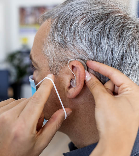 Doctor inserting hearing aid in man's ear