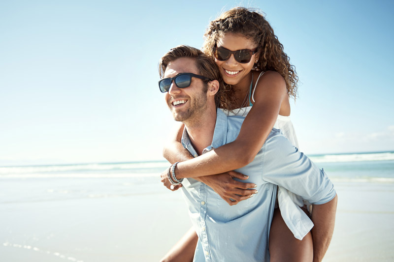 man wearing sunglasses and carrying woman along the beach