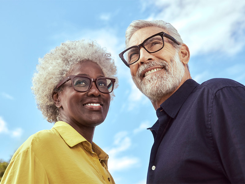 Two people wearing glasses standing outdoors against a blue sky