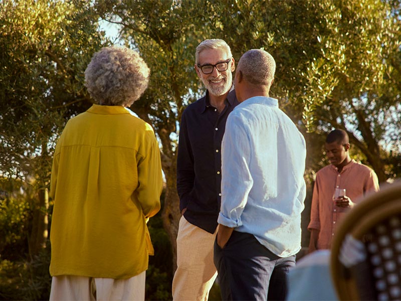 Three adults talking outdoors with trees in background
